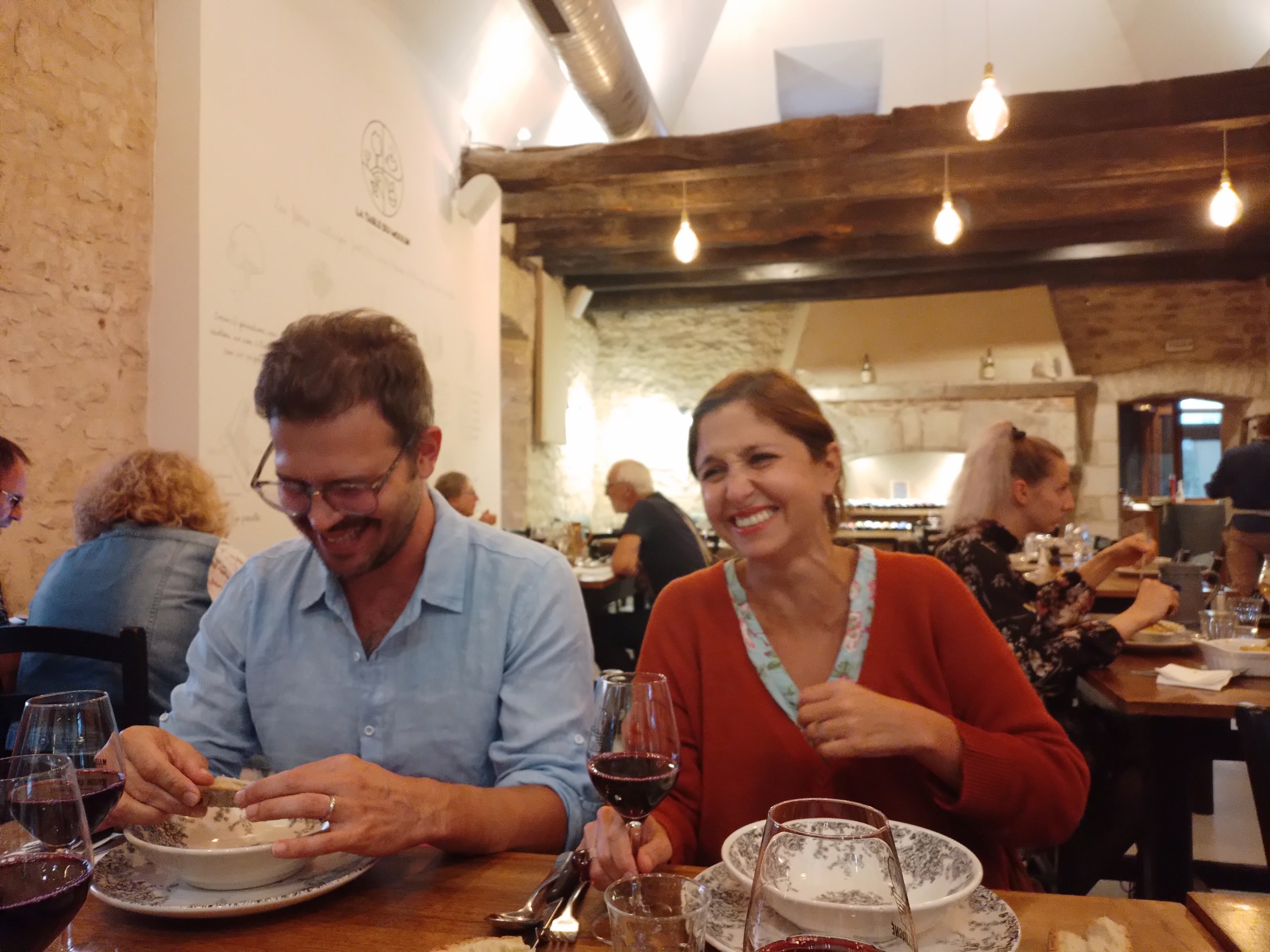 Smiling couple dining at a restaurant, enjoying wine, with a cozy interior setting.
