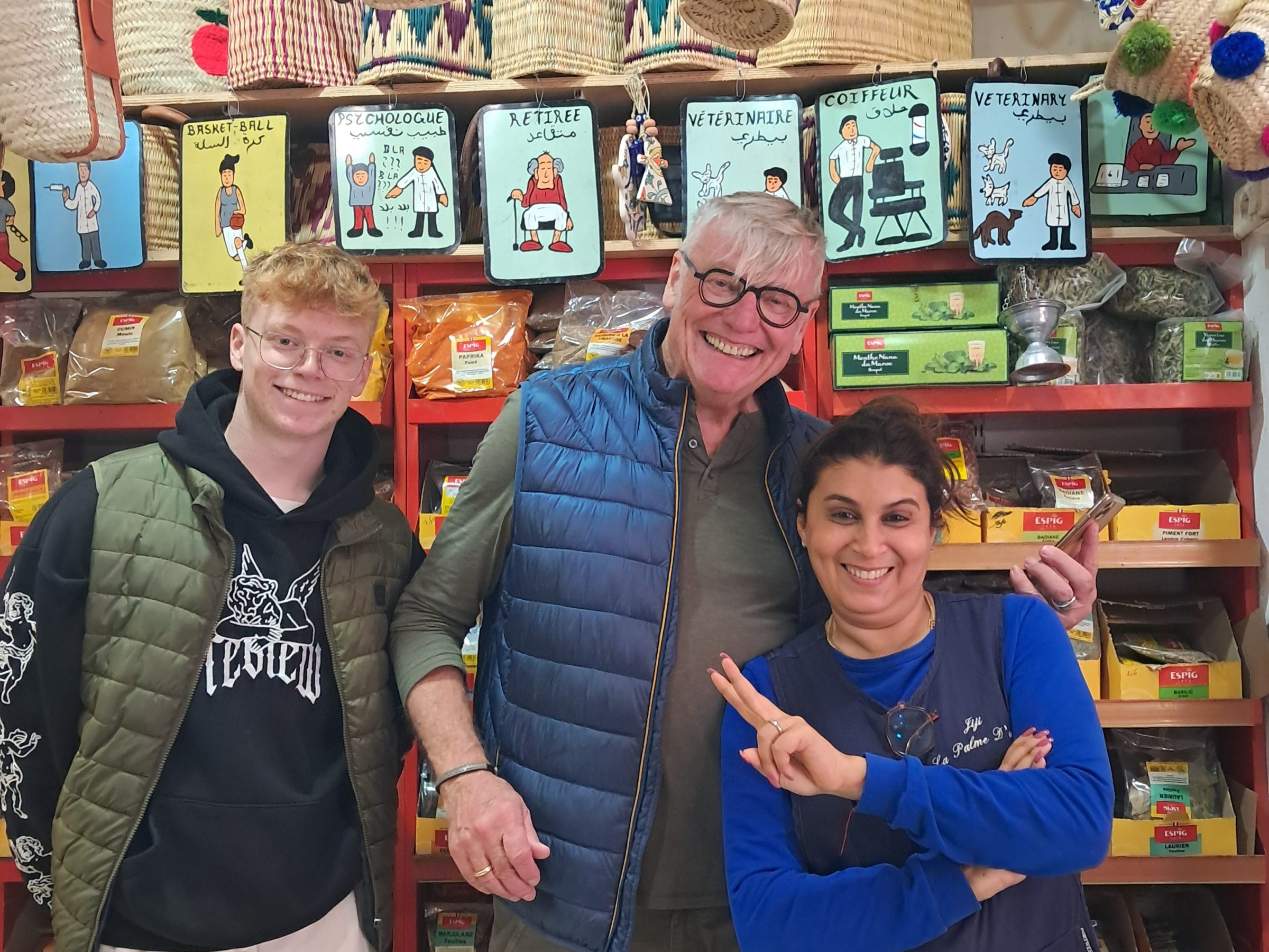 Three people smiling in a shop with baskets hanging overhead.
