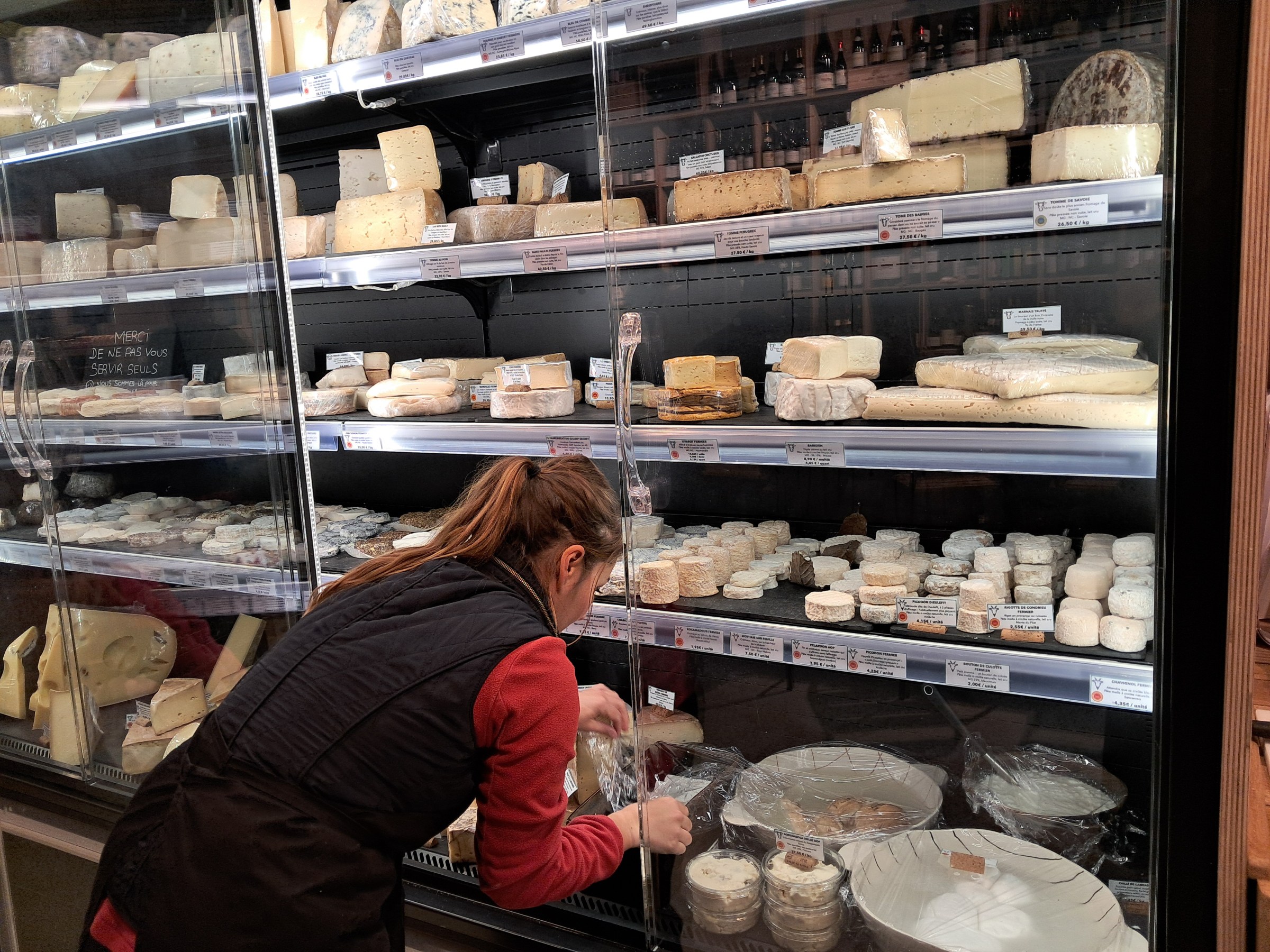 Person arranging cheese in a glass display case at a store.