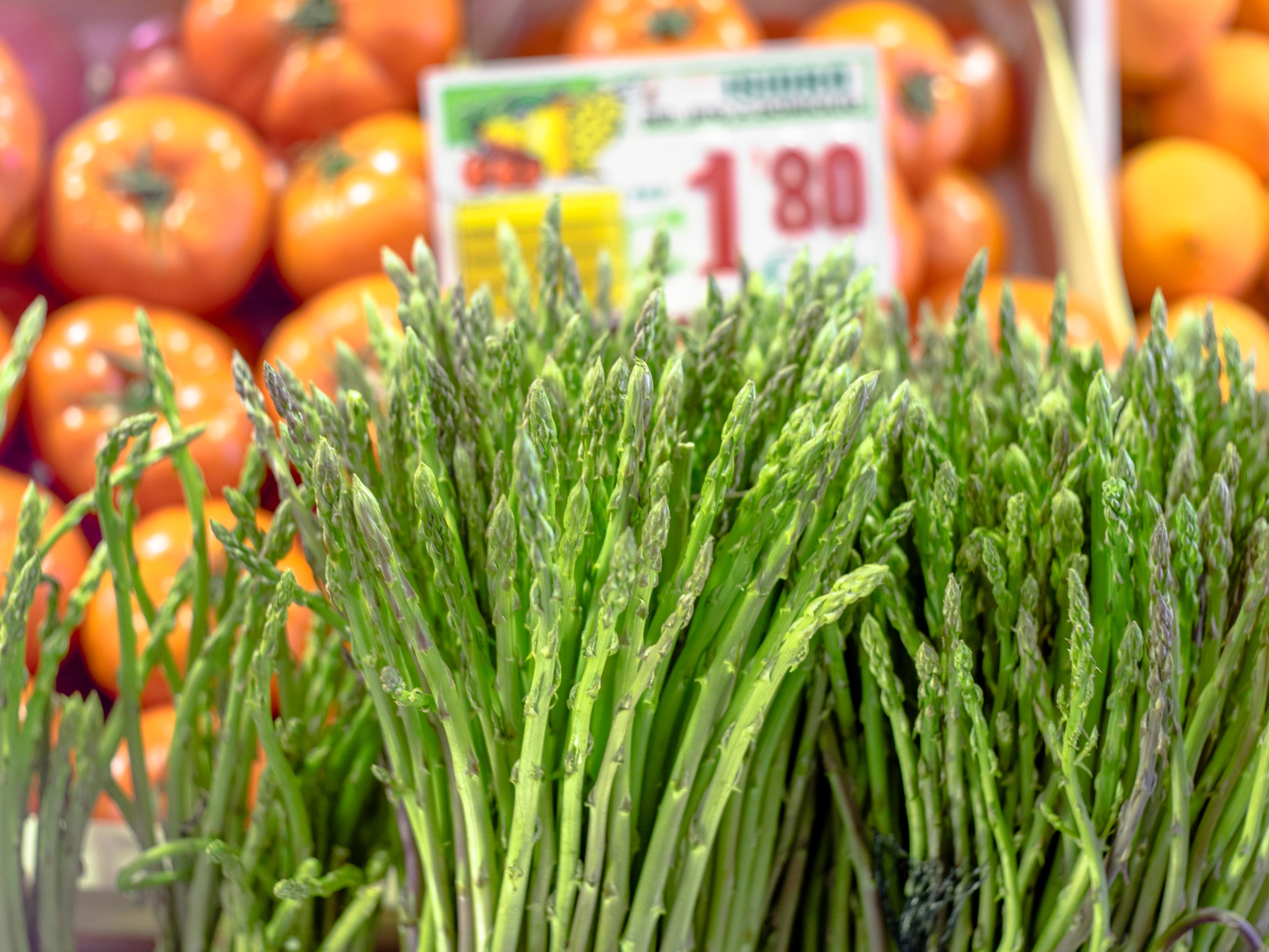 Fresh asparagus bunches displayed in front of ripe tomatoes at a market.