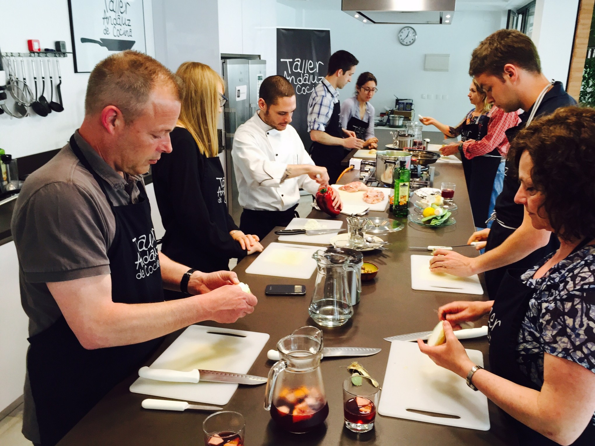 People in aprons participate in a cooking class, preparing food on a countertop.