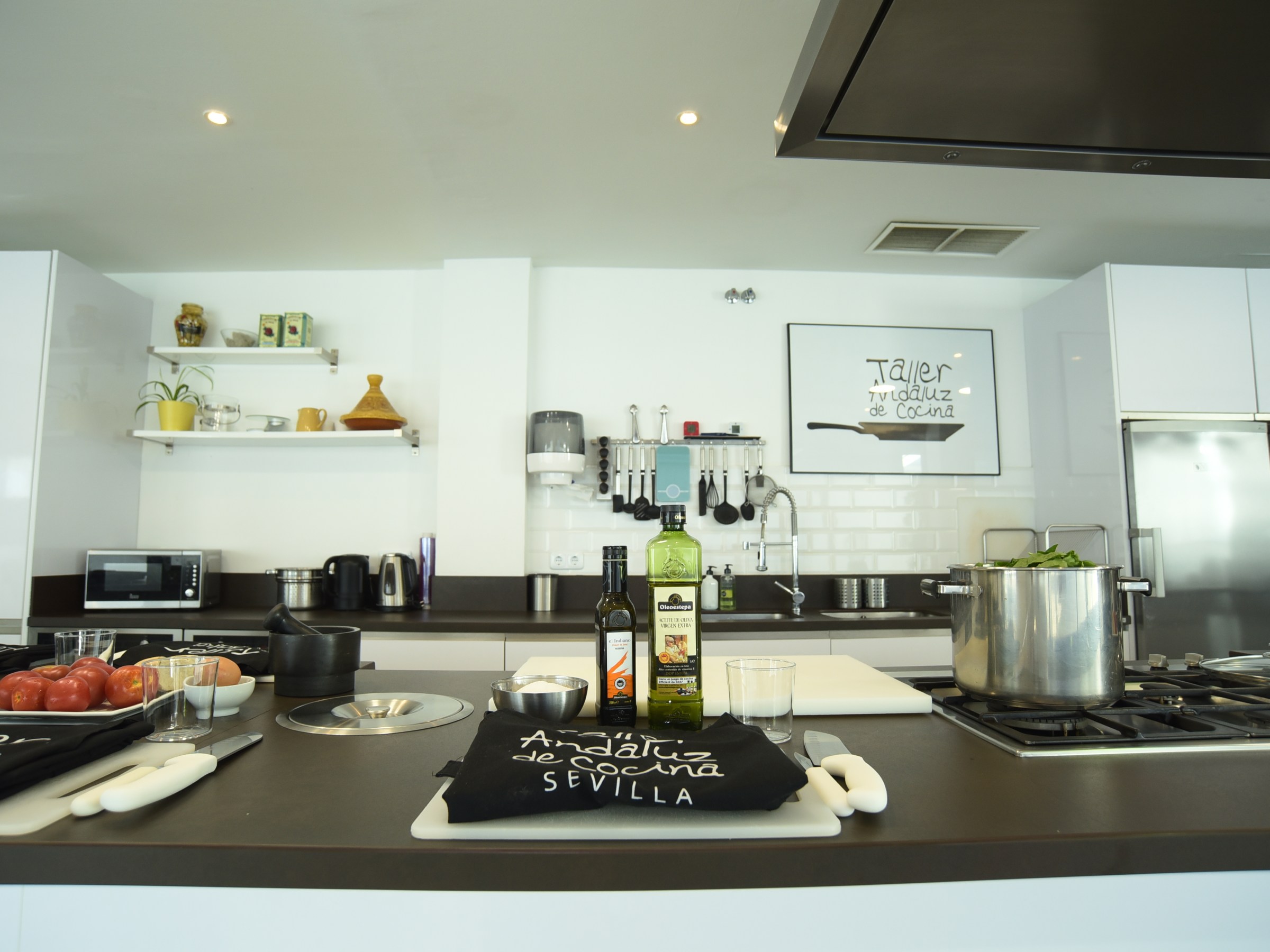 Modern kitchen with cooking class setup, featuring ingredients, utensils, and aprons on the countertop.