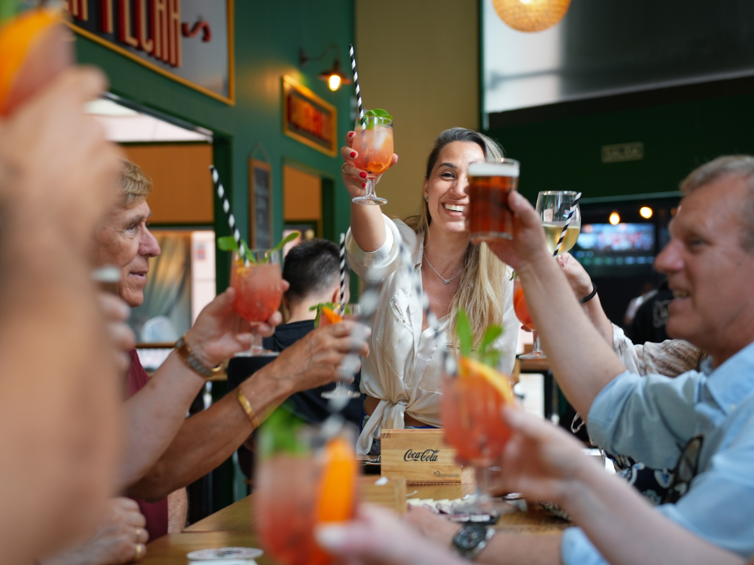 Group of people toasting with colorful drinks at a lively indoor gathering.