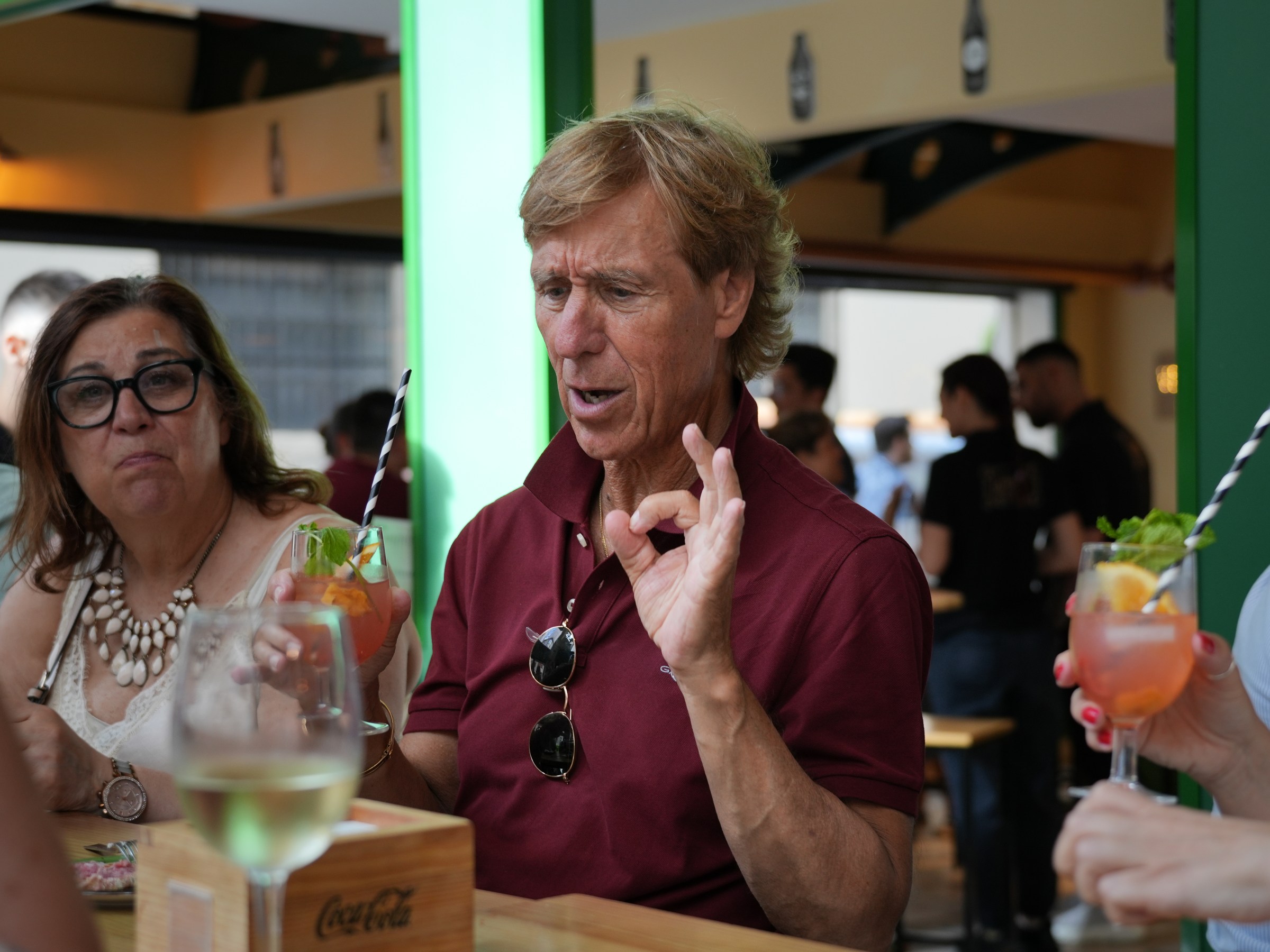 People at a bar with drinks, one person gesturing with hand, others holding cocktails.