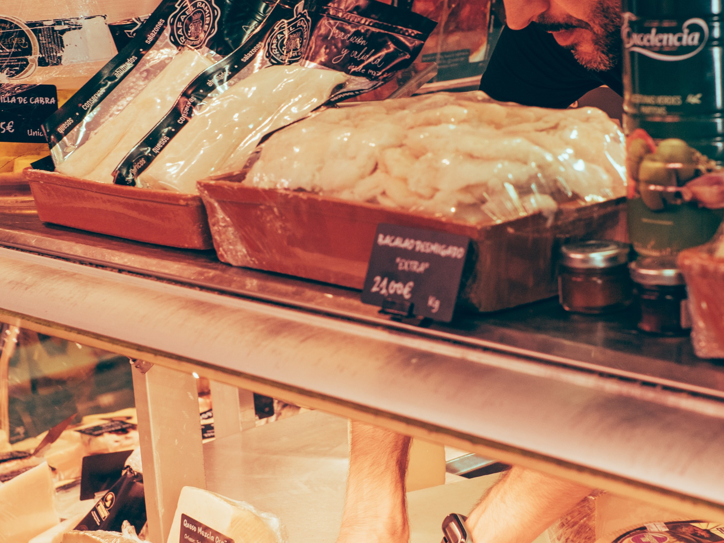 Man arranging cheese in a deli display, surrounded by various packaged cheeses.