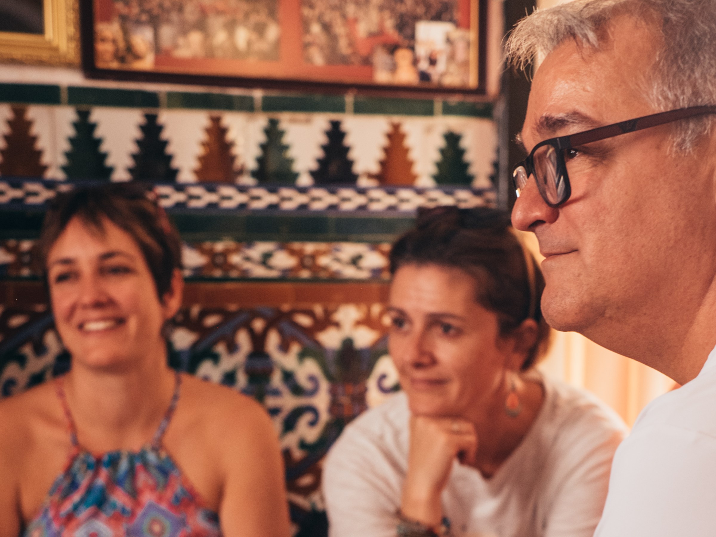 Three people sitting indoors with decorative tiles on the wall behind them.