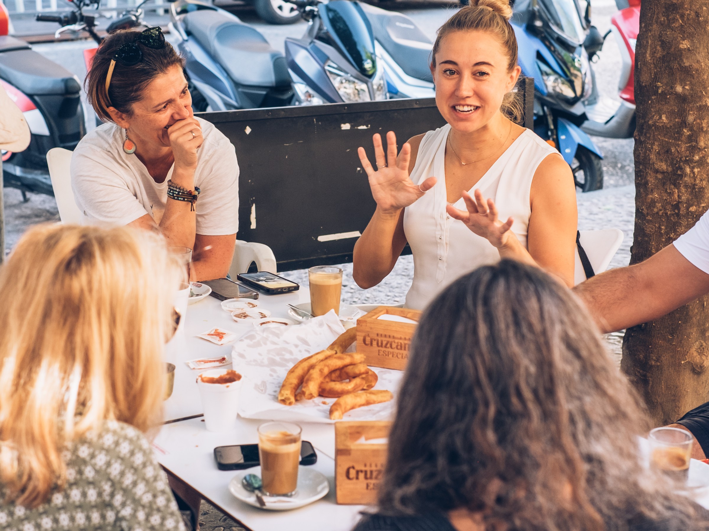Group of people having coffee and pastries at an outdoor table.