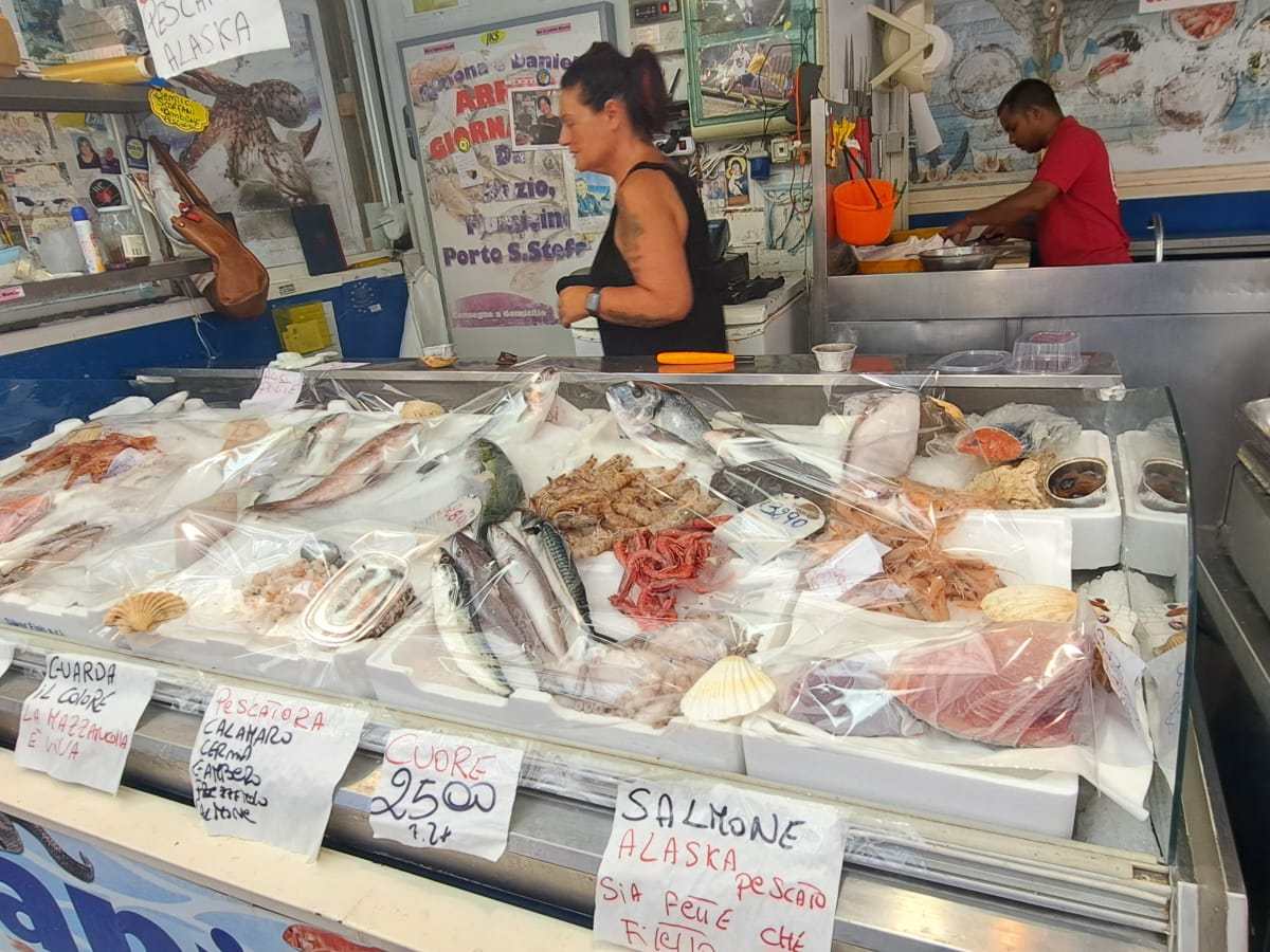 Seafood market stall with various fish and shellfish displayed on ice, with two people in the background.