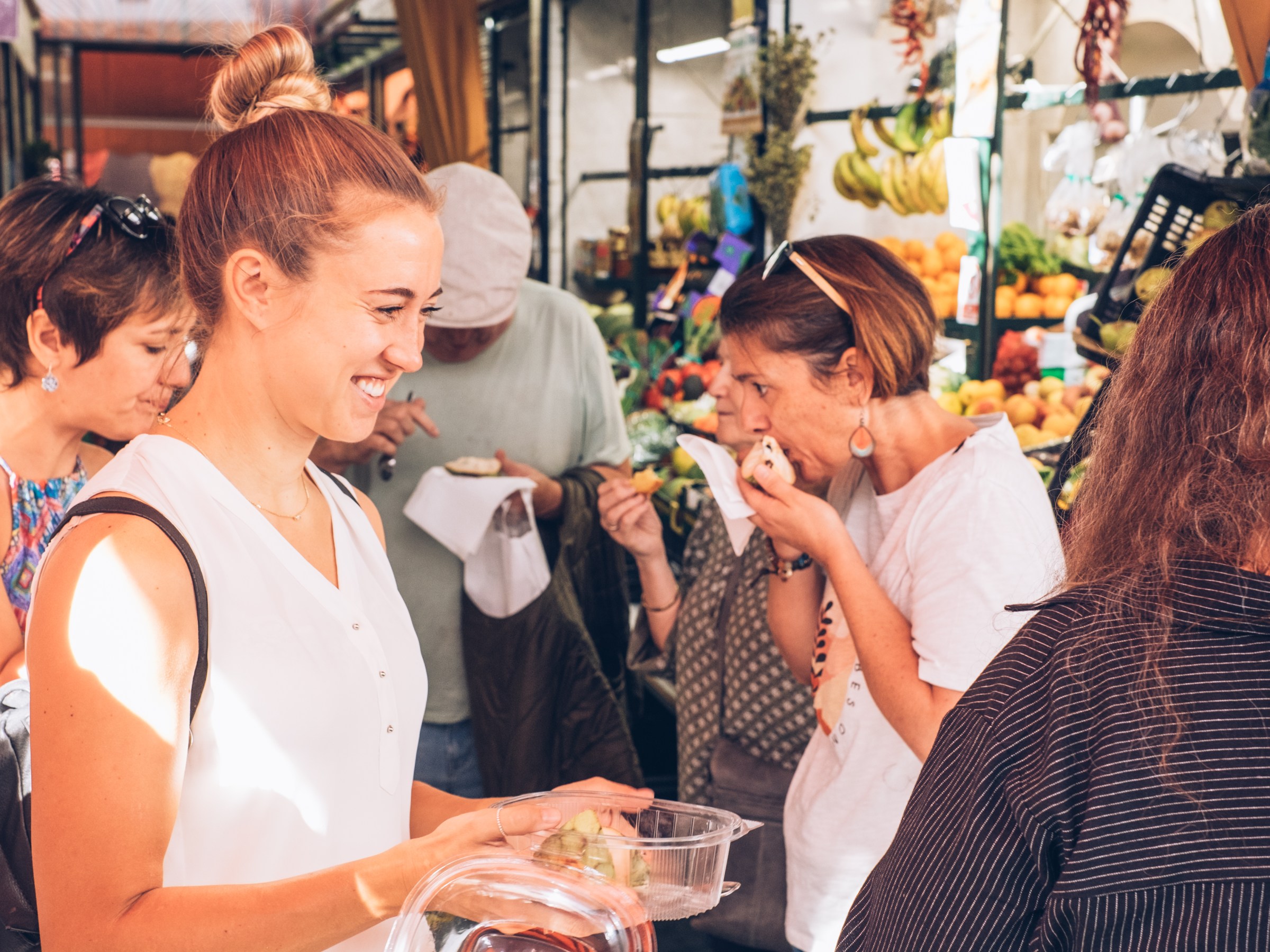People shopping at an outdoor market, with fruits and vegetables visible in the background.