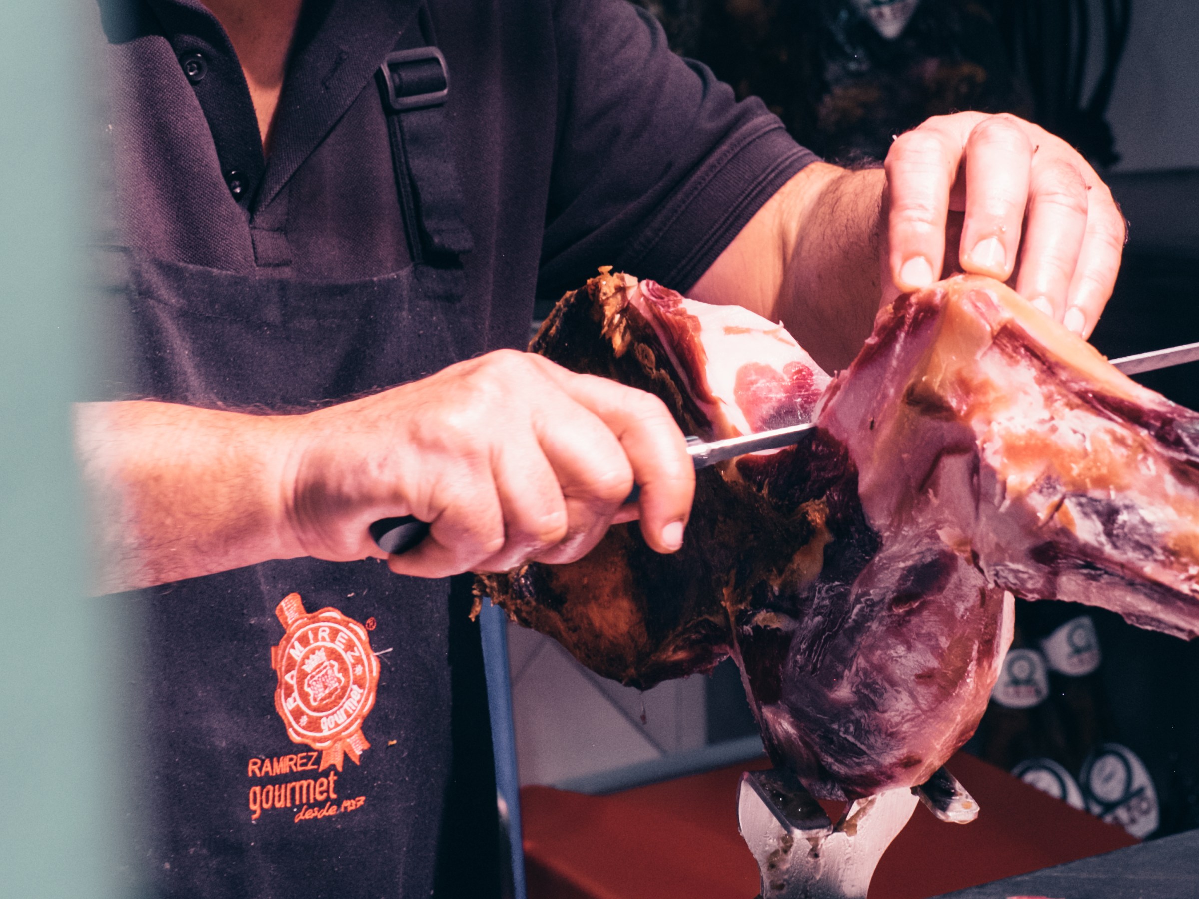 Person slicing cured ham with a knife, wearing a black apron.