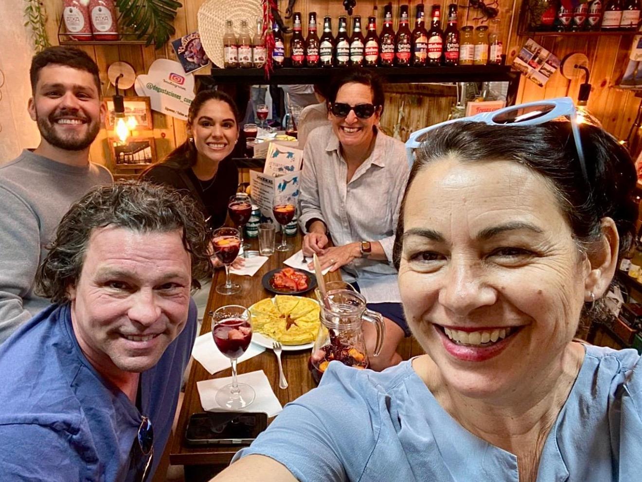 Group of five people smiling at a table with drinks and food in a cozy bar setting.
