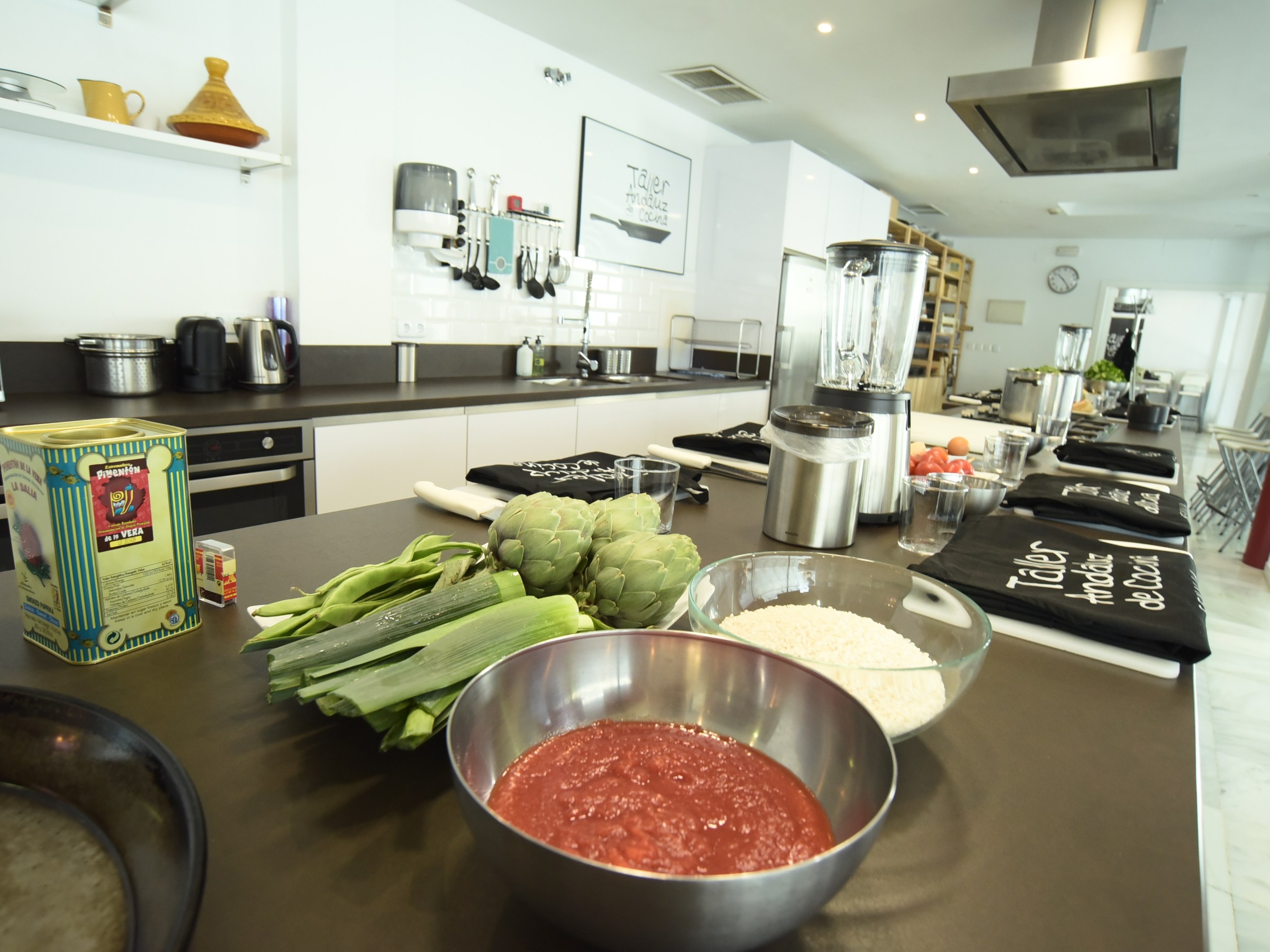 Kitchen with cooking ingredients like tomatoes, leeks, artichokes, and rice on a counter.