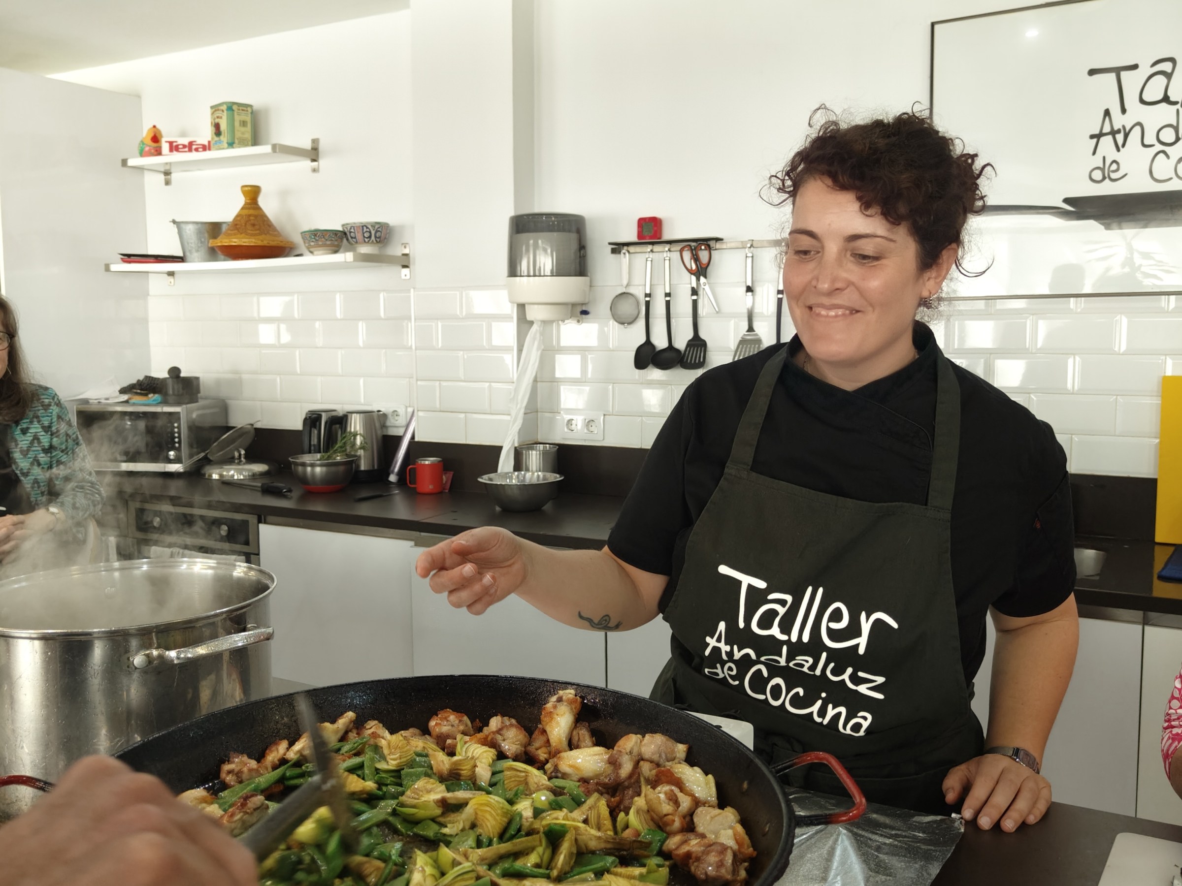 Woman cooking and smiling in a kitchen wearing a culinary workshop apron.