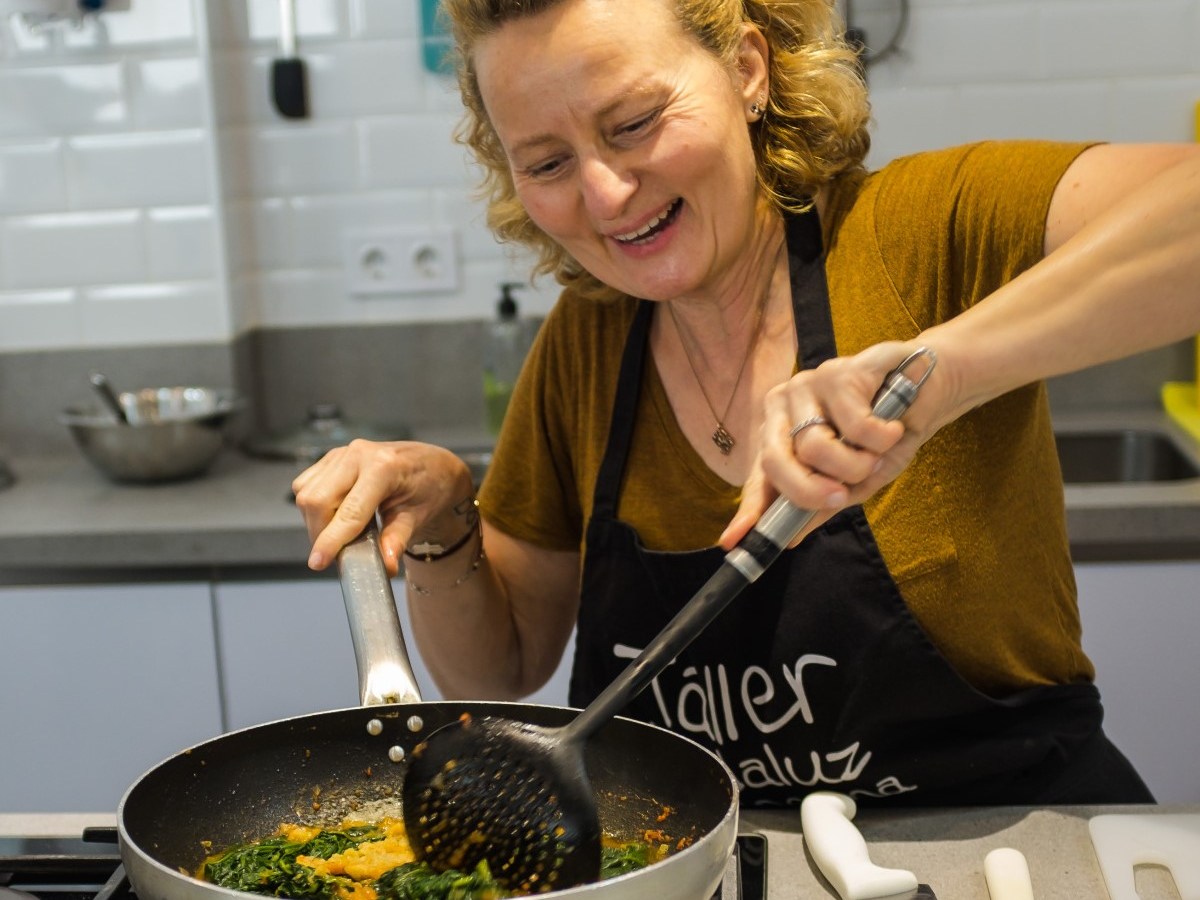 Woman smiling while cooking spinach in a pan on a stove.