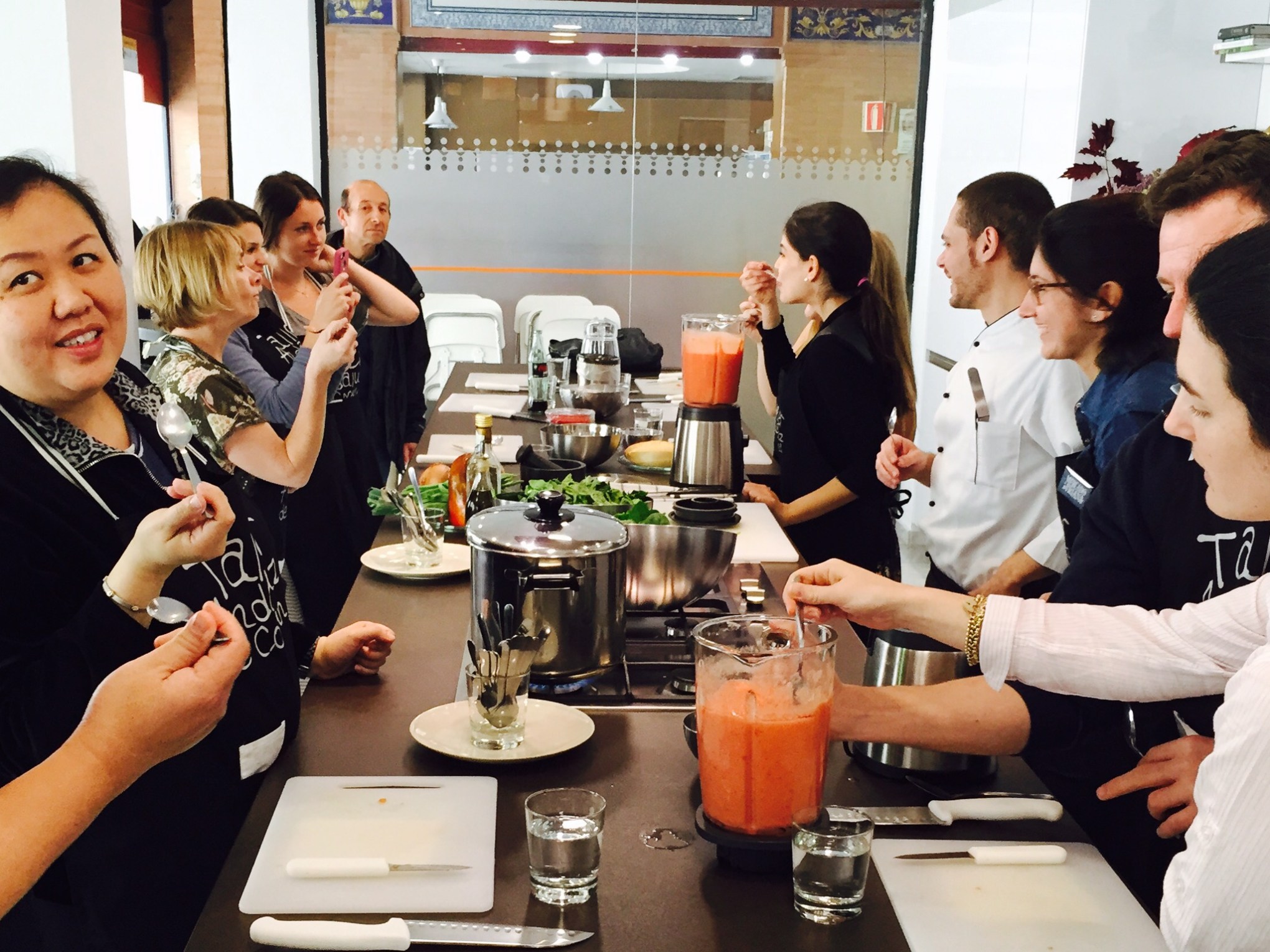 Group cooking class participants around a countertop with blenders and ingredients.