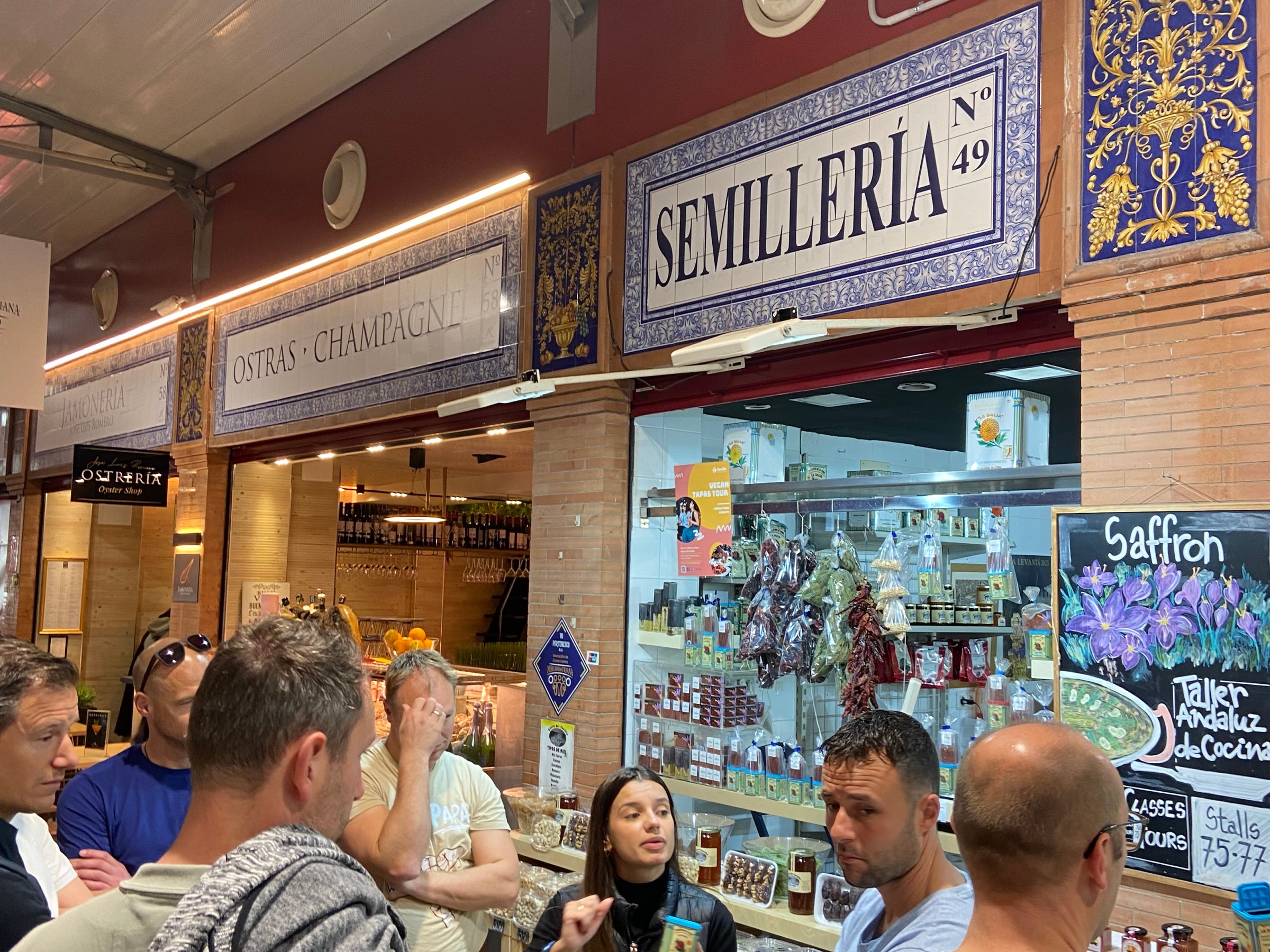 People gathered near a market stall labeled 'Semillería' with various goods displayed.