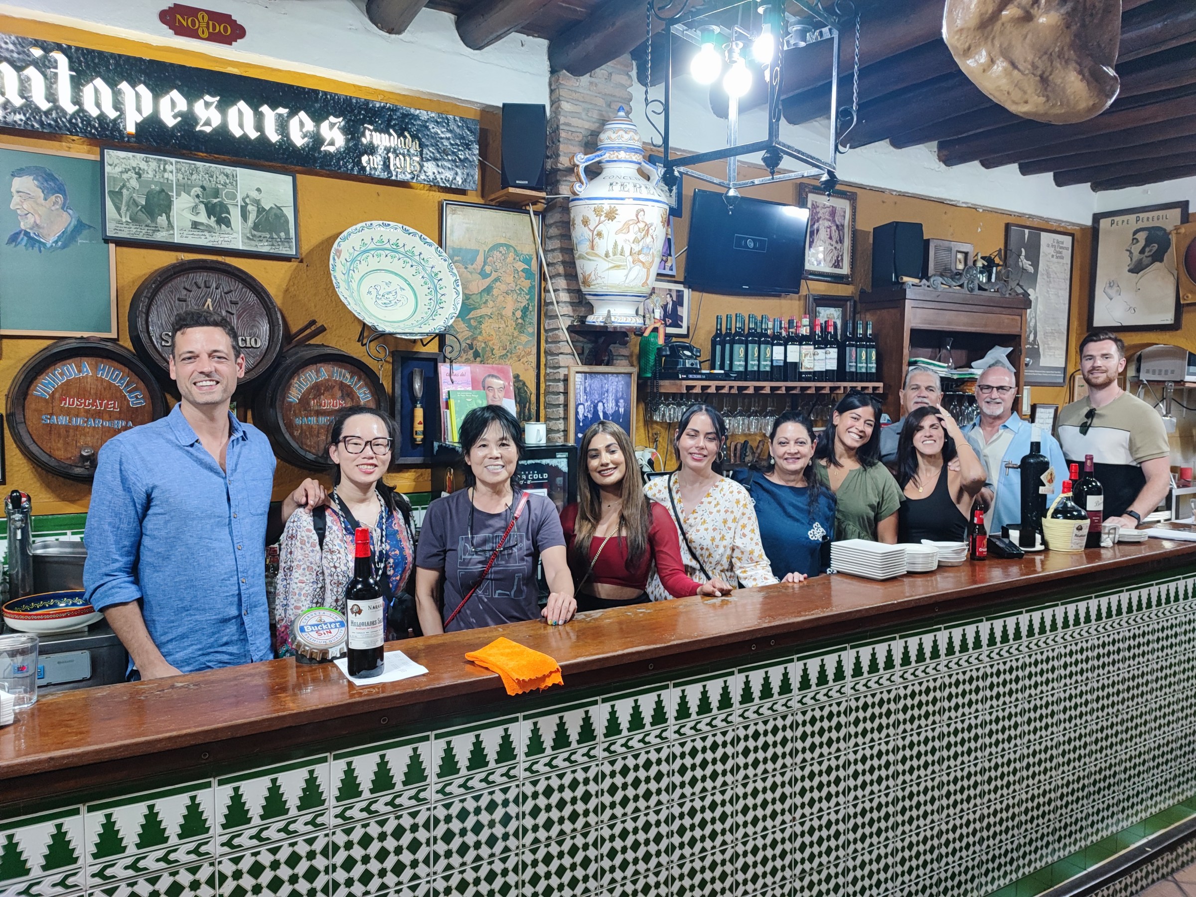 Group of people smiling behind a bar counter in a rustic setting with decorated plates and wine bottles.