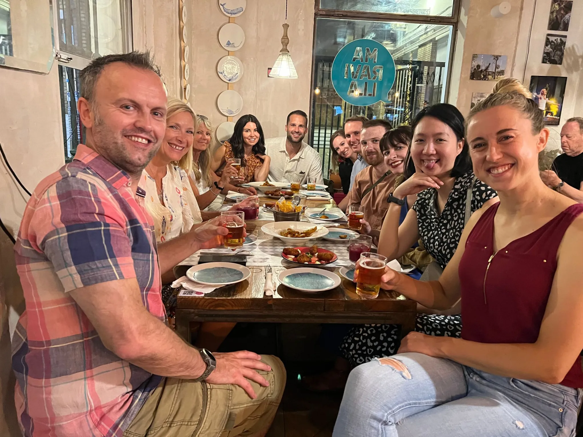 A group of people smiling around a table with food and drinks in a cozy restaurant.