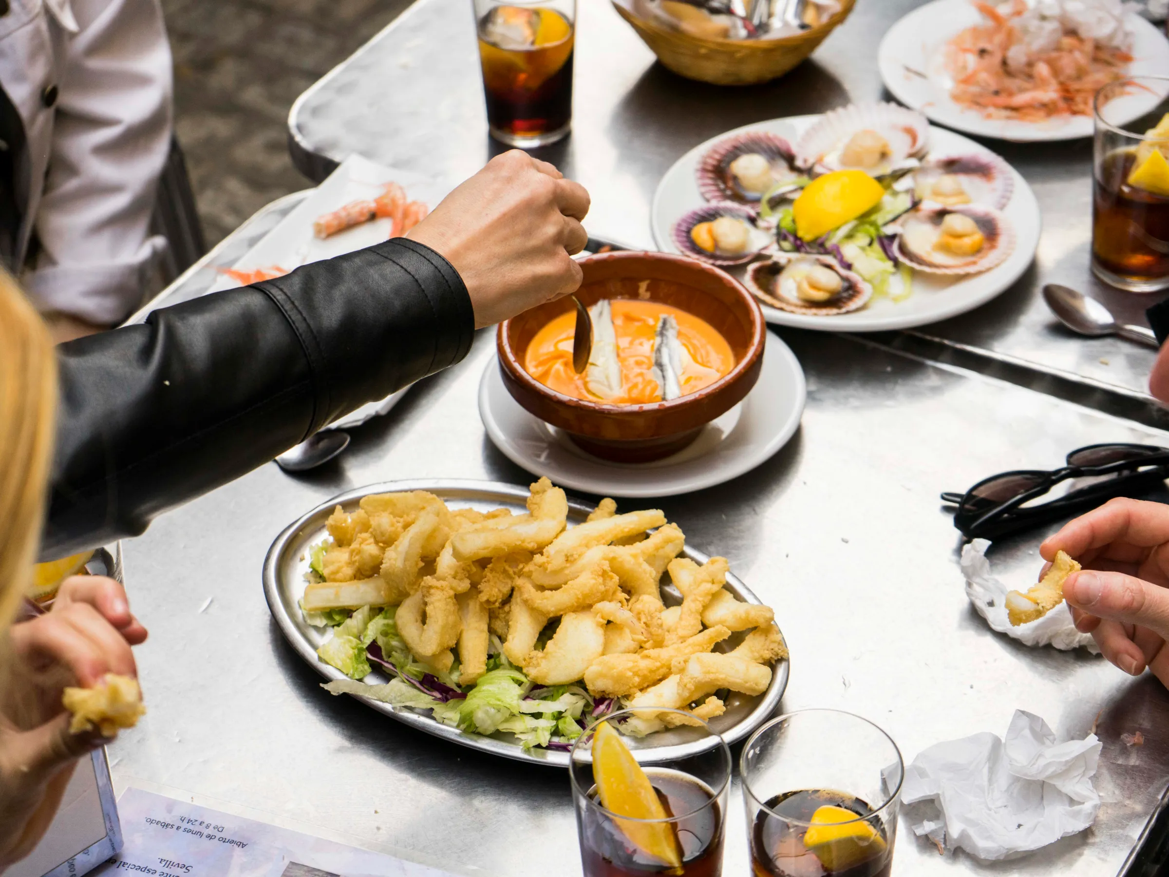 People dining on fried calamari, soup, scallops, and drinks at an outdoor table.