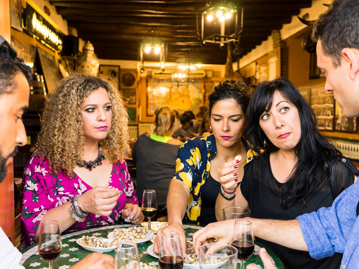 Group of people at a table with drinks and snacks, engaged in conversation.