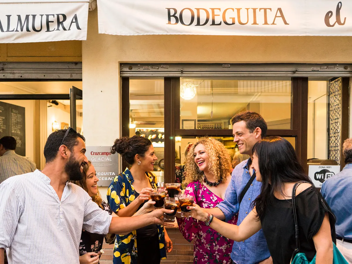 Group of people laughing and toasting drinks outside a bodega.