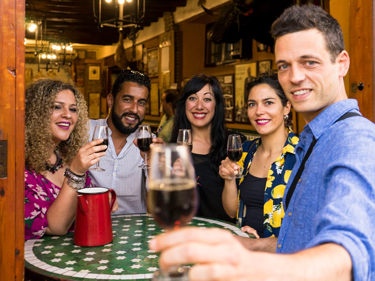 Group of five people raising wine glasses, smiling inside a cozy restaurant.