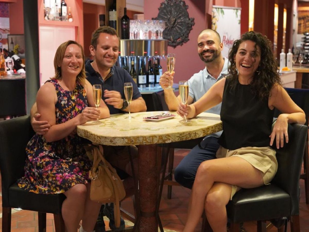 Four people sitting at a table in a bar, smiling and holding glasses of champagne.