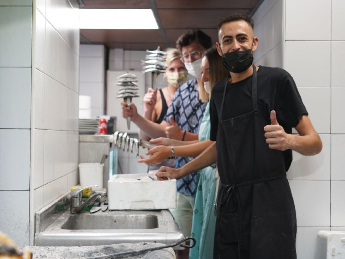 Group of smiling people in a kitchen, one person giving a thumbs up wearing a mask and apron.