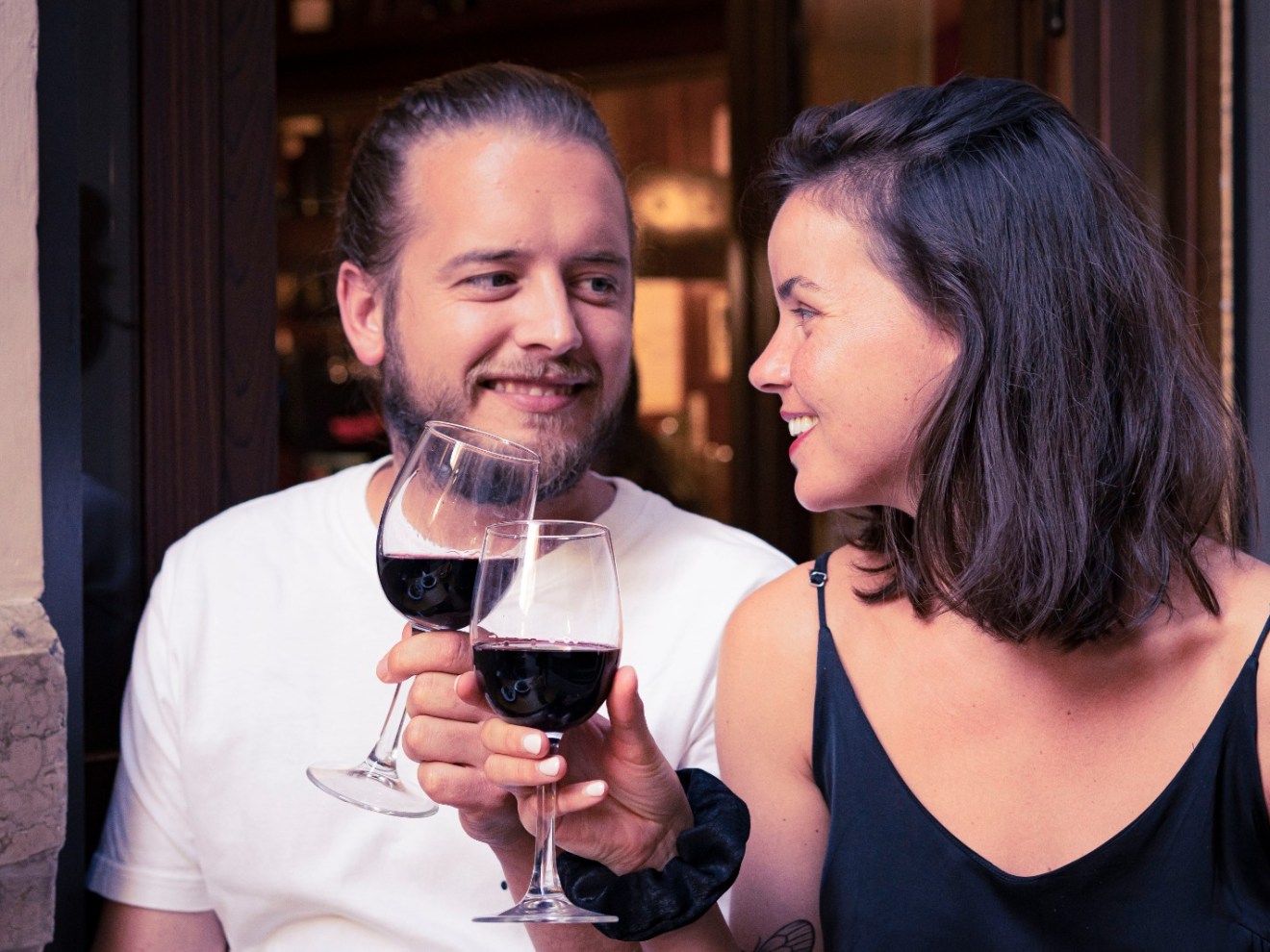Smiling couple clinking wine glasses outside a bar.