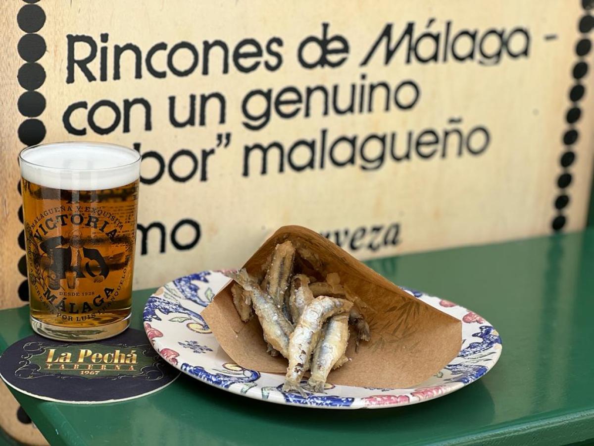 Glass of beer beside a plate of fried fish on a floral dish.