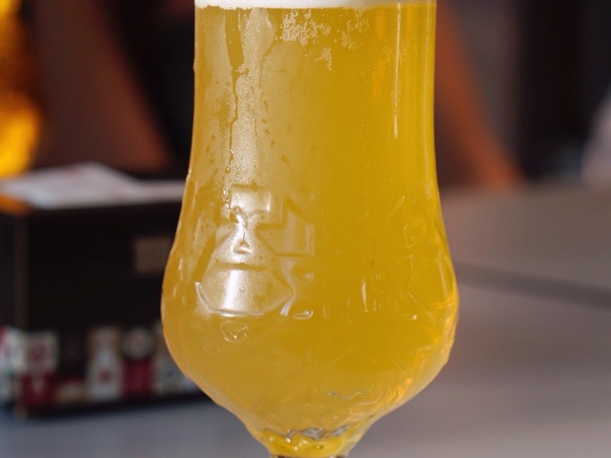 Tulip glass of pale beer with frothy head on a table.