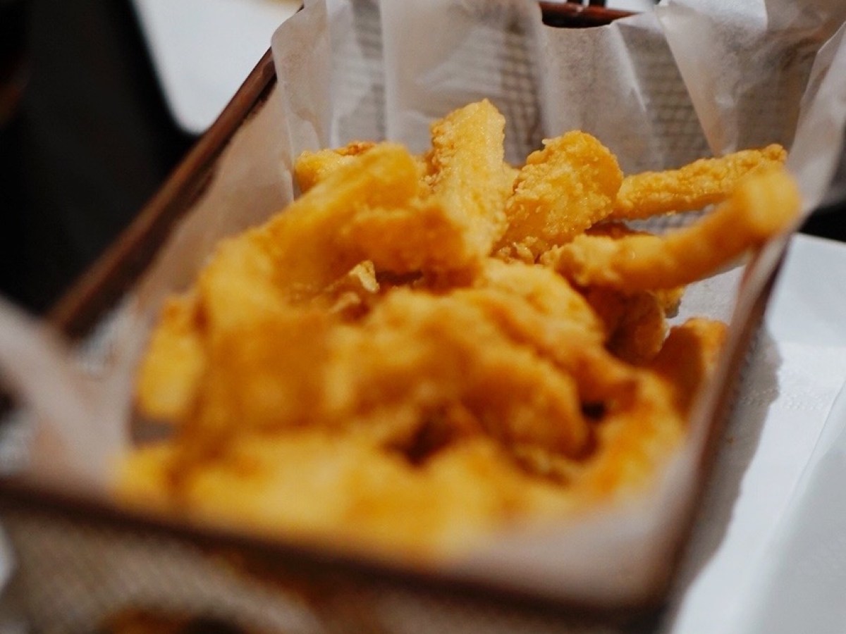Basket of fried calamari with lemon wedge and dip in the foreground.