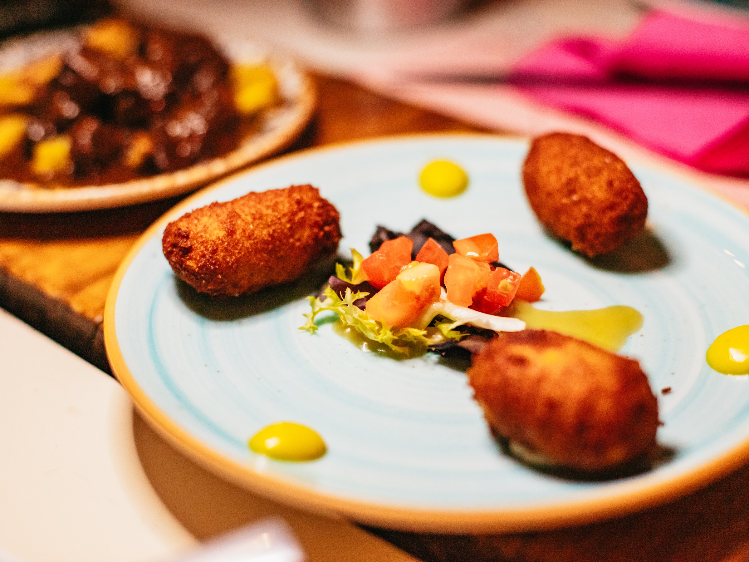 Three croquettes on a plate with diced vegetables and sauce.