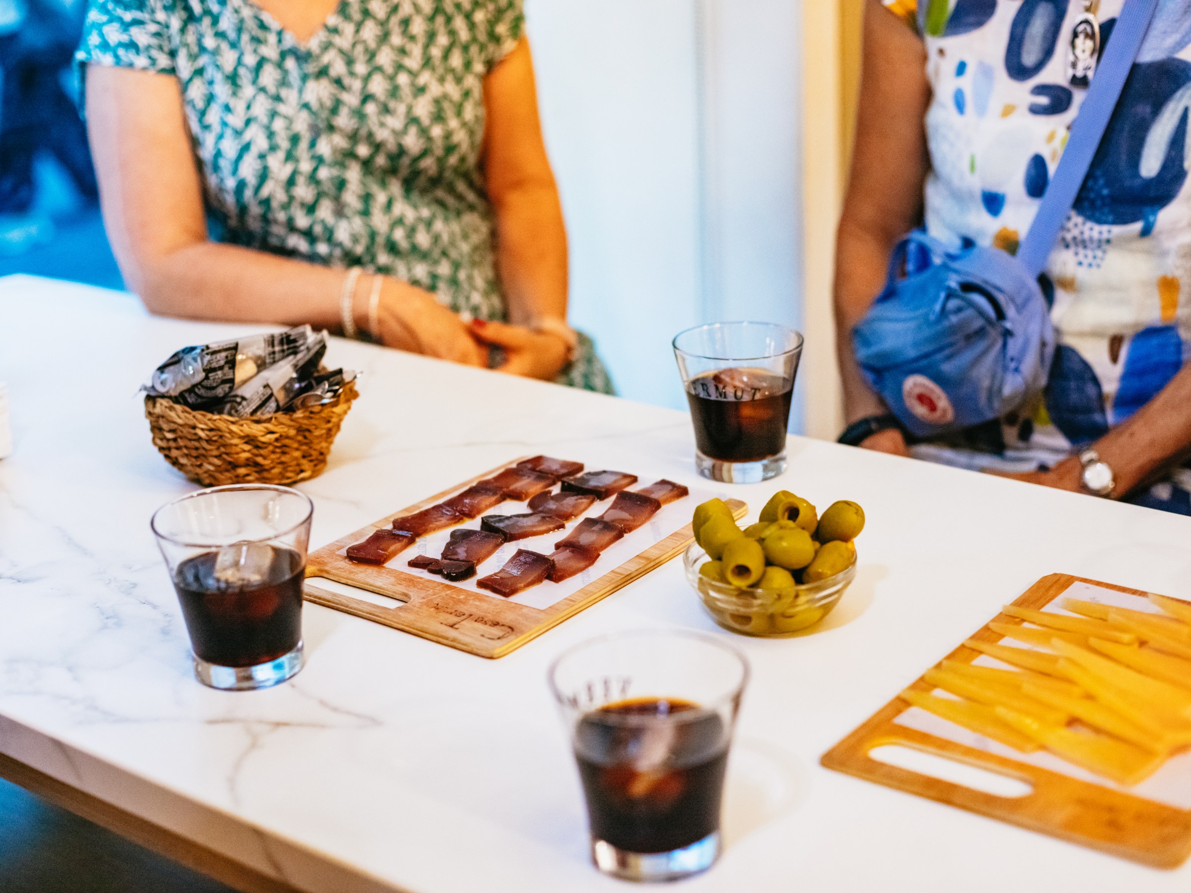 Table with snacks and drinks, including olives, cheese, and glasses of dark beverage.