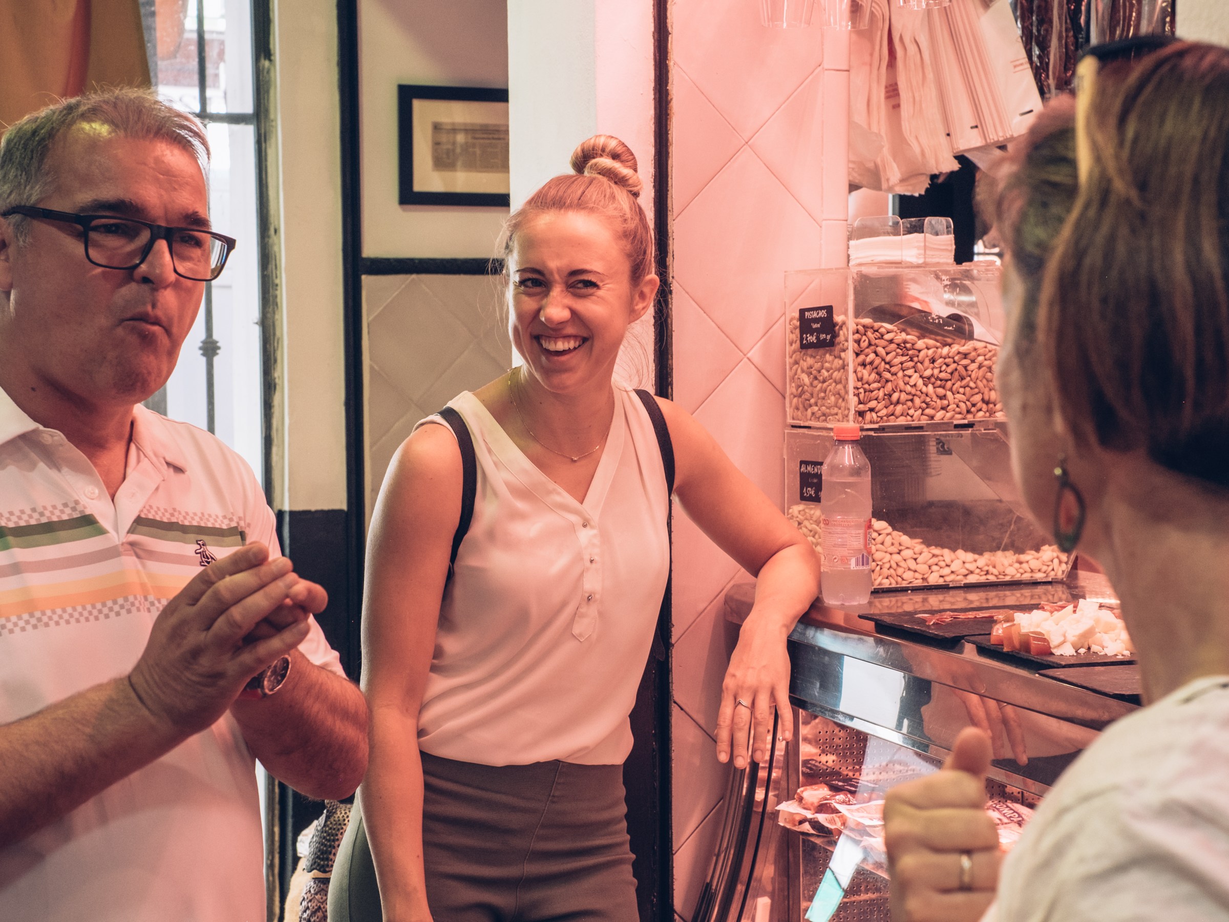 Three people socializing and smiling at a market near a nut display.
