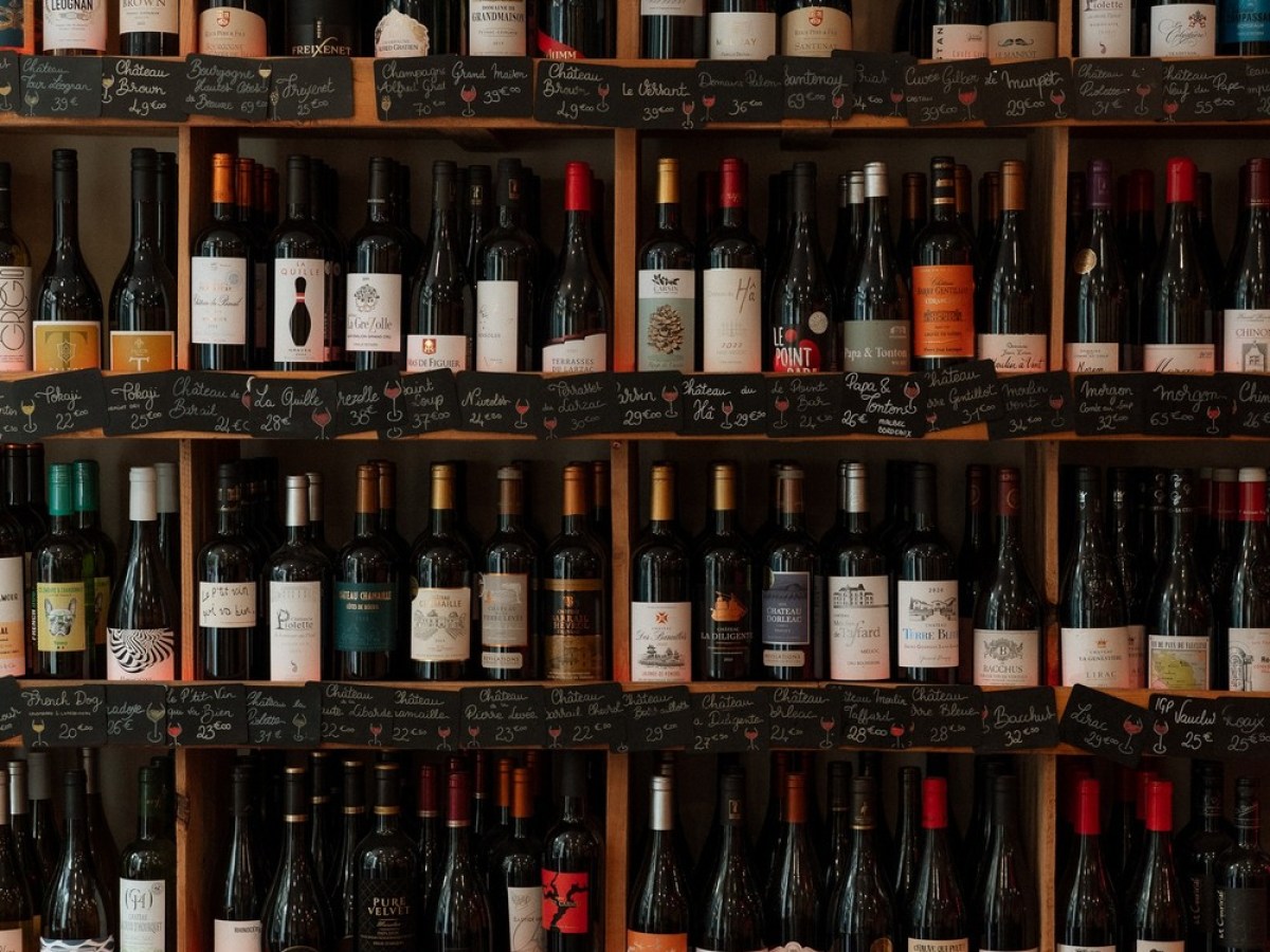 a bottle of beer next to a book shelf filled with wine glasses