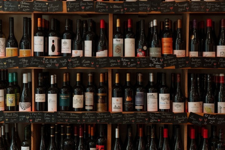 a bottle of beer next to a book shelf filled with wine glasses