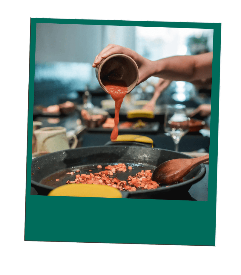 Hand pouring sauce from bowl into pan with chopped ingredients.