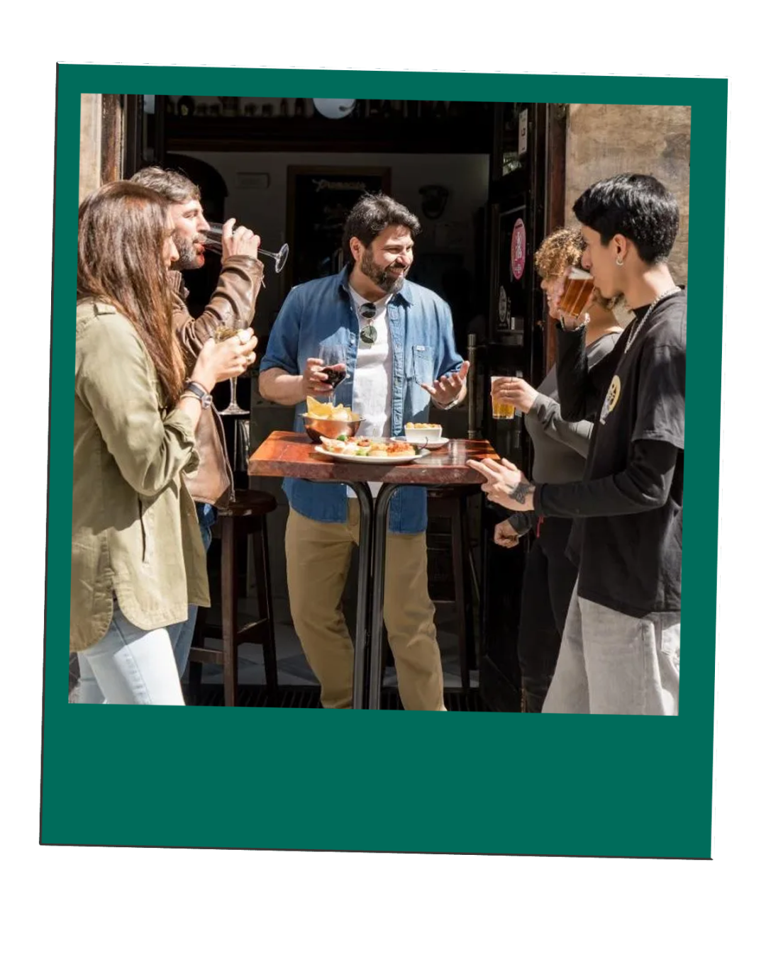 Five people standing around a high table with drinks and snacks outside a café.