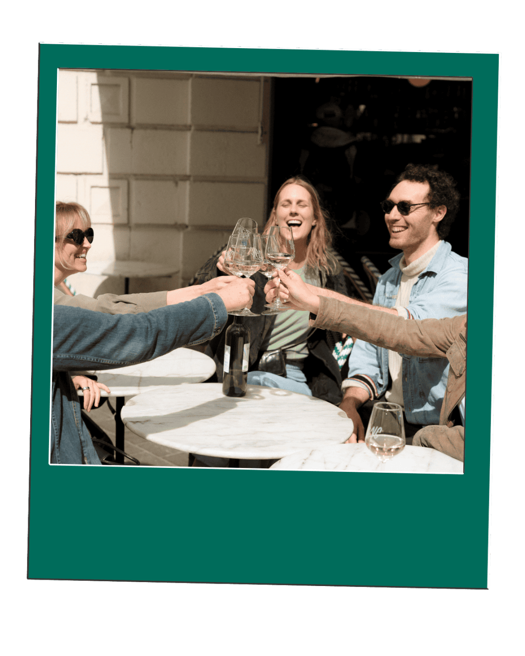 Four people smiling and toasting with wine glasses at an outdoor table.