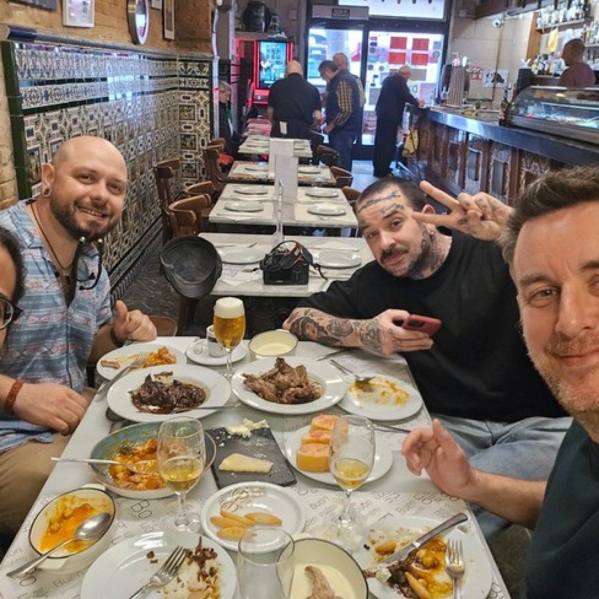 Four men smiling at a restaurant table with various dishes and drinks.