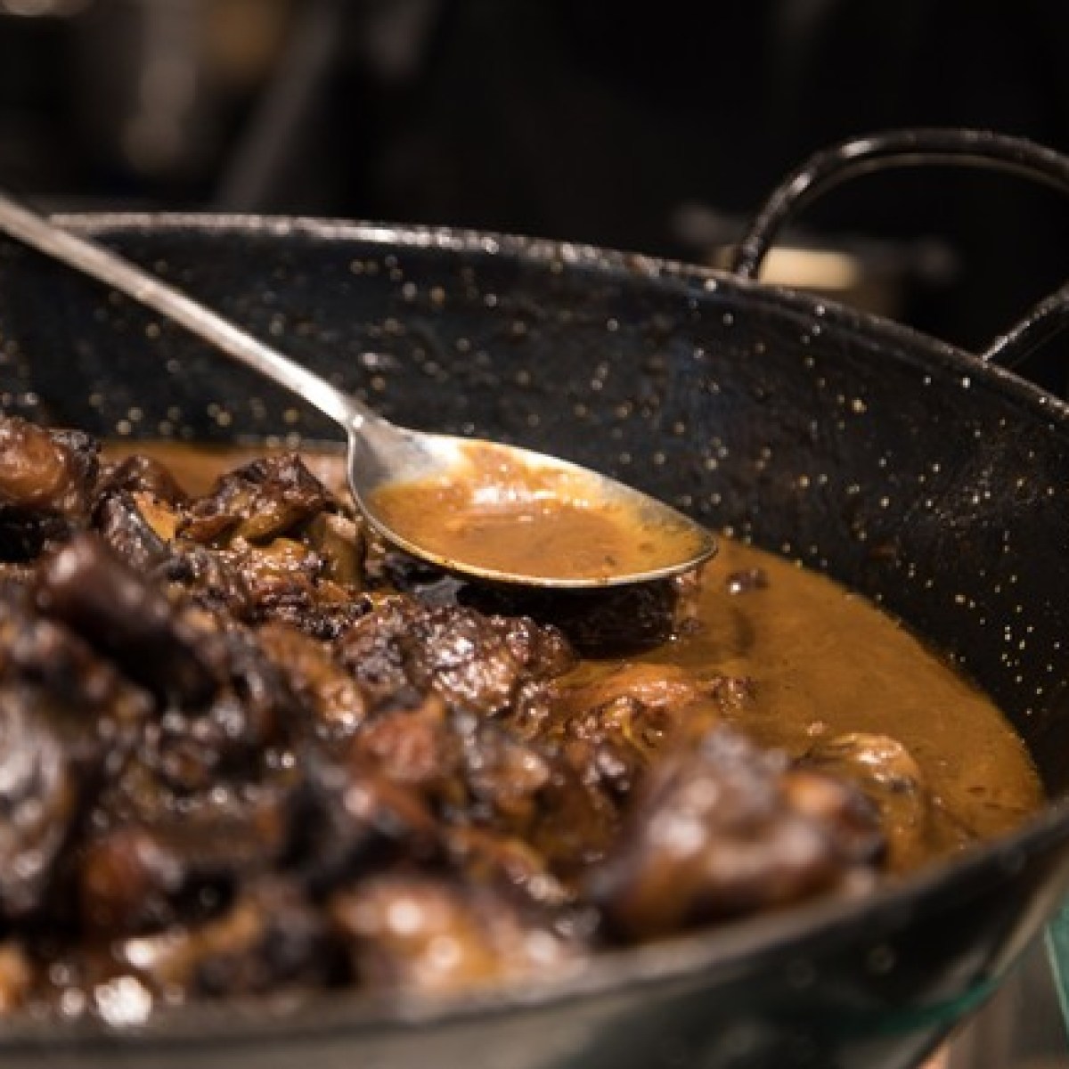 Close-up of a stew with meat in a pan, a spoon resting on the side.