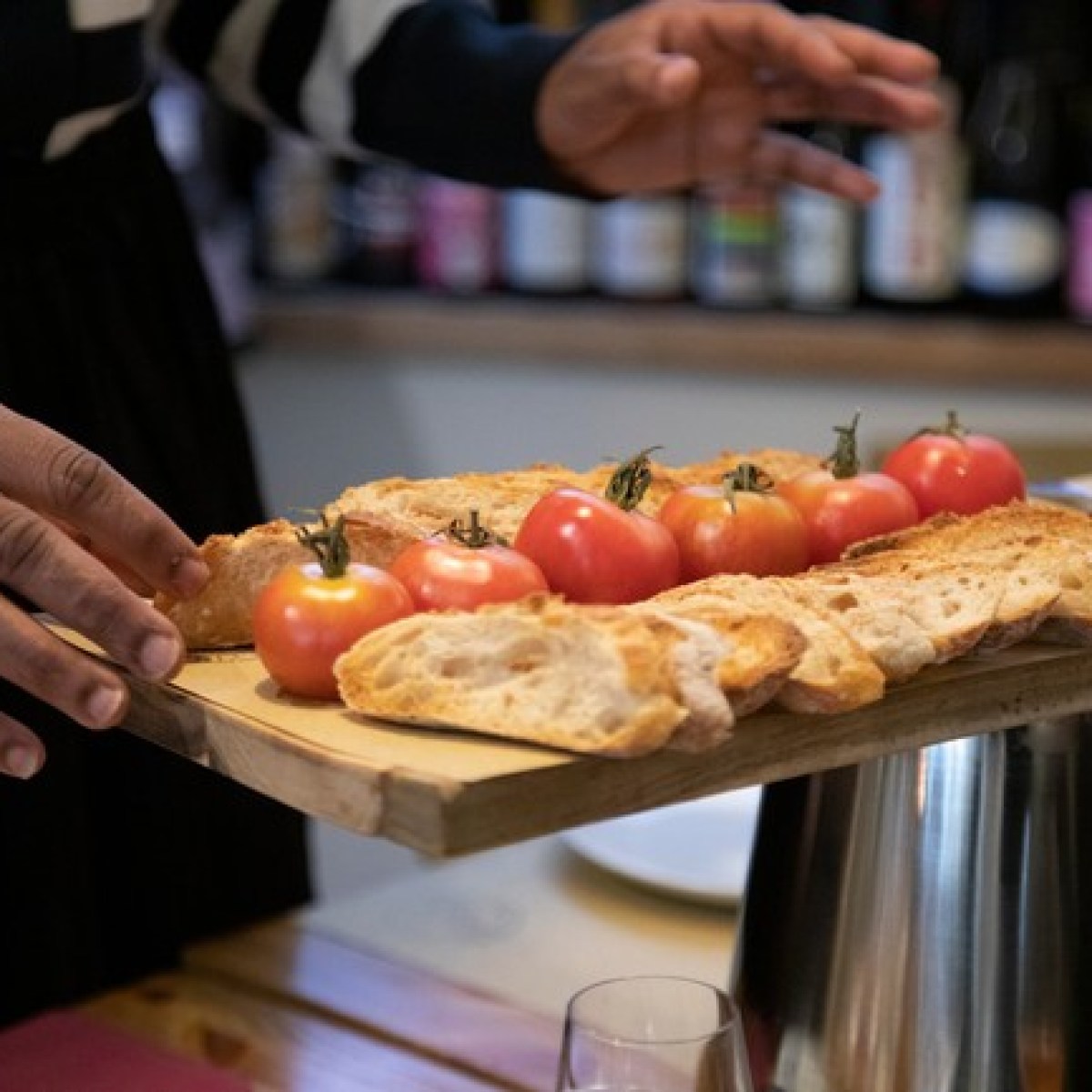 Person holding a wooden tray with sliced bread and tomatoes.