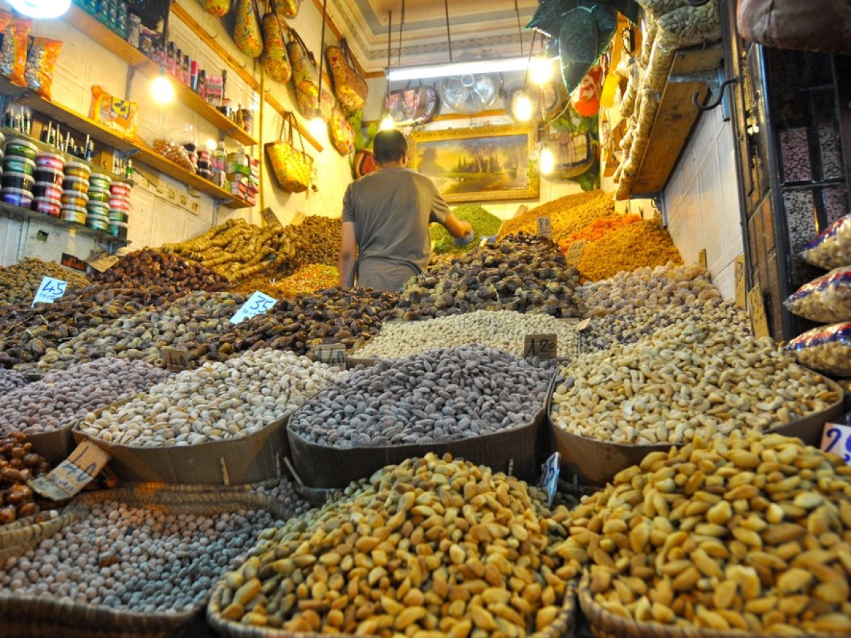 Market stall displays various nuts and dried fruits with a seller organizing items.