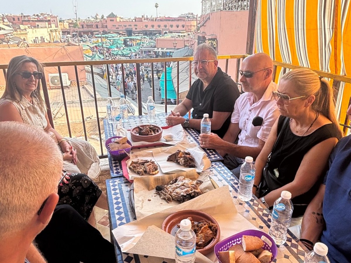 People dining on a rooftop with views of a bustling market and buildings in the background.