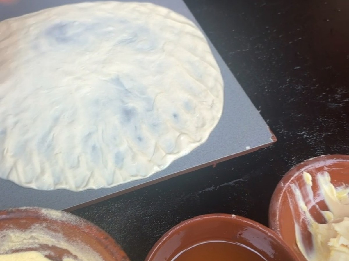 Person preparing flat dough on a board, surrounded by bowls of flour, sauce, and butter.