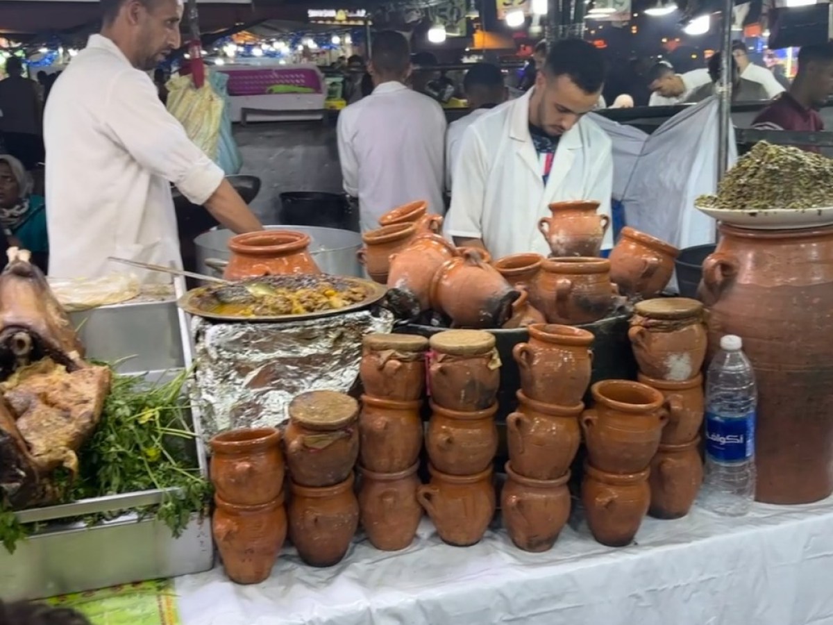Market stall with stacked clay pots and food, busy vendors in background.