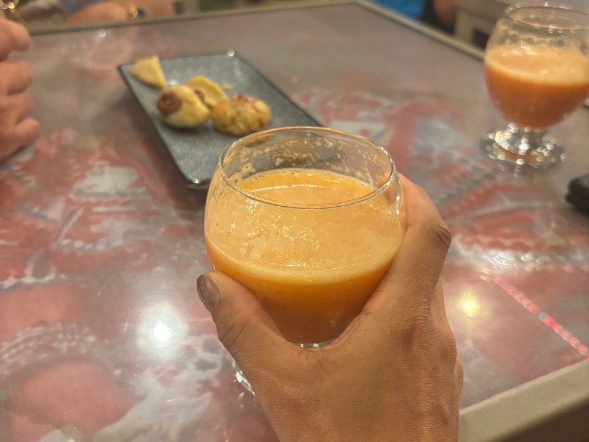 Hand holding an orange drink in a glass at a table with snacks and other drinks.