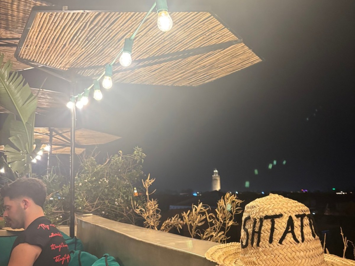 Outdoor seating with string lights, straw hat on ledge, and night city view.