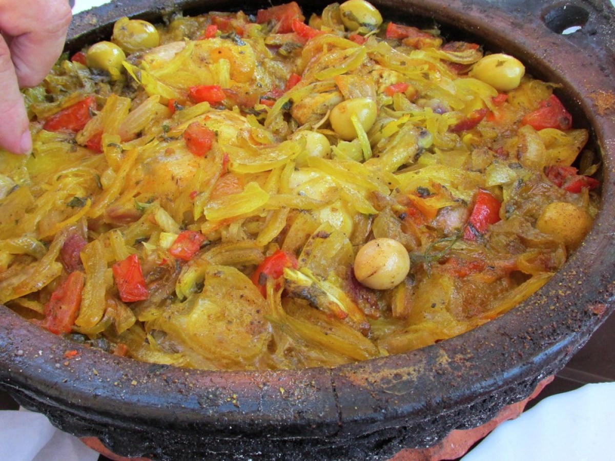 Close-up of a colorful dish with vegetables and olives in a rustic clay pot.